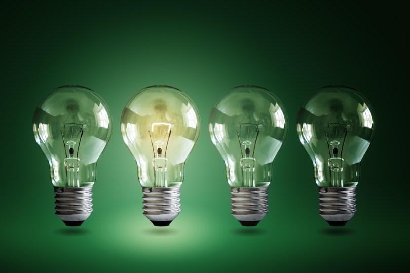 Illuminated light bulb in a row of dim bulbs on a green background
