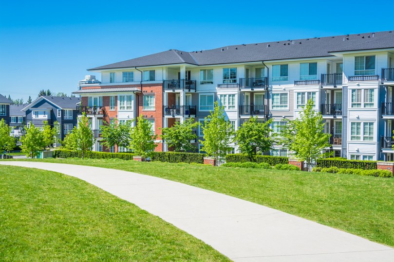 Residential apartment building on sunny day with blue sky, concrete walkway and lawn in front