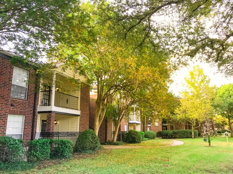 Typical 2-story apartment complex building in fall season. Grassy lawn patio yard and autumn yellow dry leaves falling on the pathway at sunset